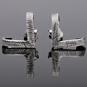 May include: A pair of silver earrings with a textured, geometric design. The earrings are shaped like a curved L.