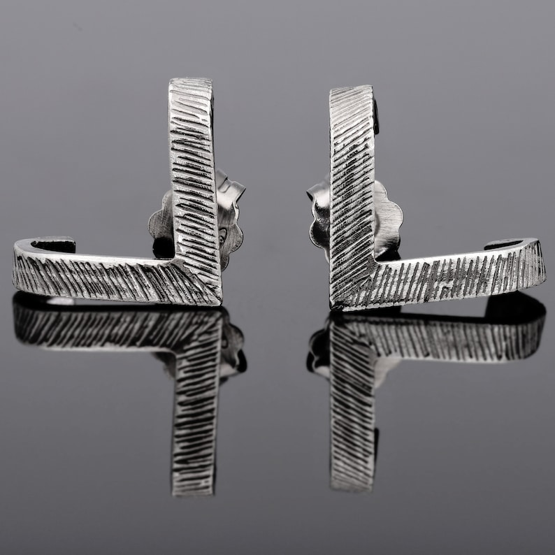 May include: A pair of silver earrings with a textured, geometric design. The earrings are shaped like a curved L.