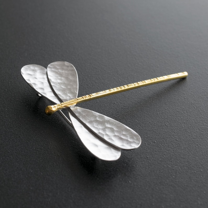 Pode incluir: Um broche de lib&eacute;lula de prata com textura martelada e corpo dourado. As asas s&atilde;o delicadas e intrincadas.