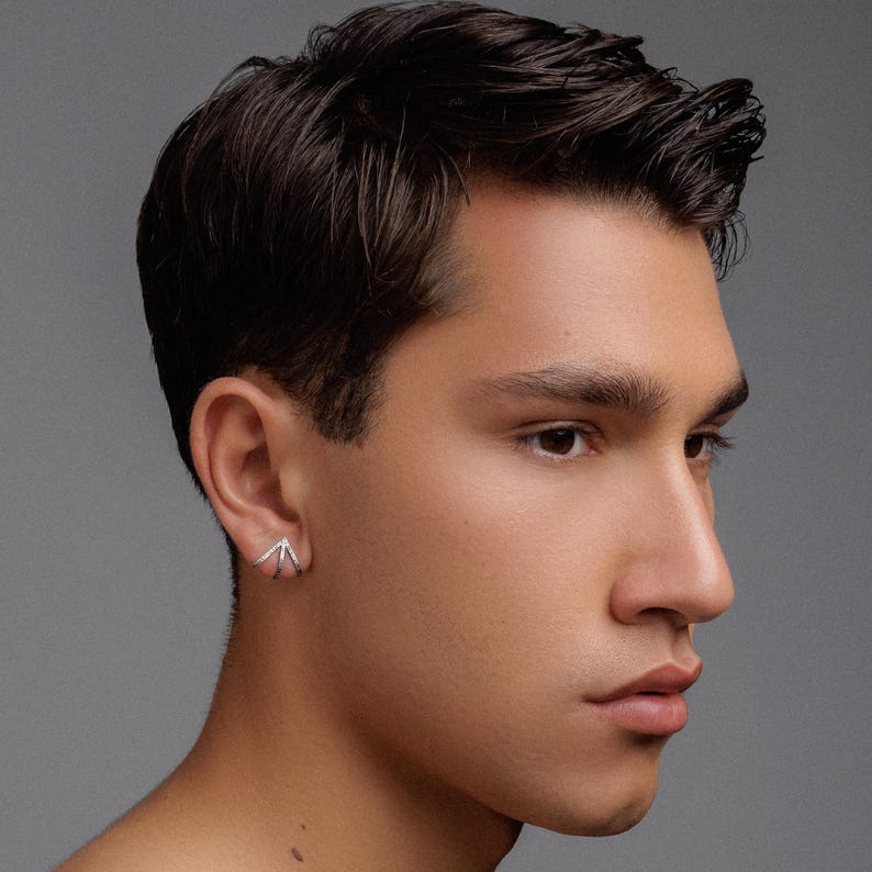 May include: A close-up of a person's ear with a silver earring in the shape of a triangle with three points.