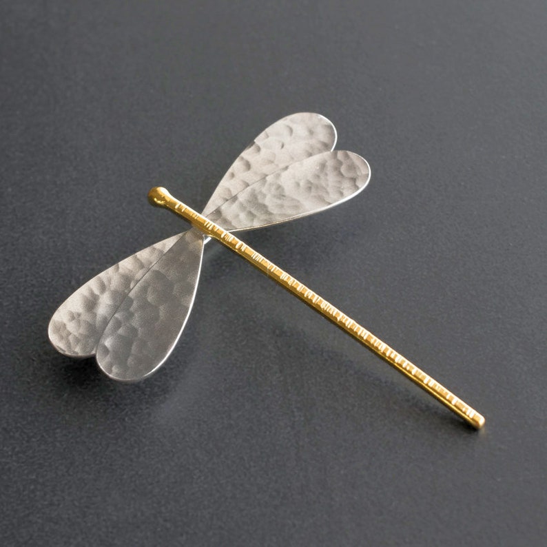 Pode incluir: Um broche de lib&eacute;lula de prata com textura martelada e corpo dourado. As asas t&ecirc;m a forma de um cora&ccedil;&atilde;o.