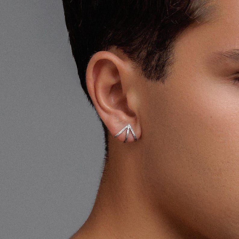 May include: A silver ear cuff with a geometric design. The cuff is made of multiple thin bands that form a V-shape.