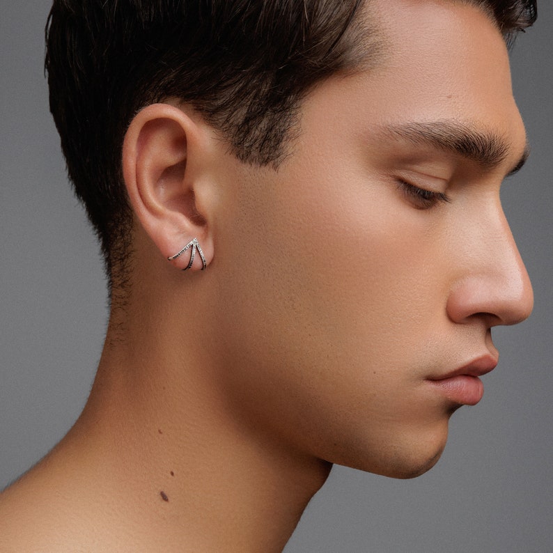 May include: A close-up of a person's ear with a silver earring featuring multiple curved bars with small diamonds.