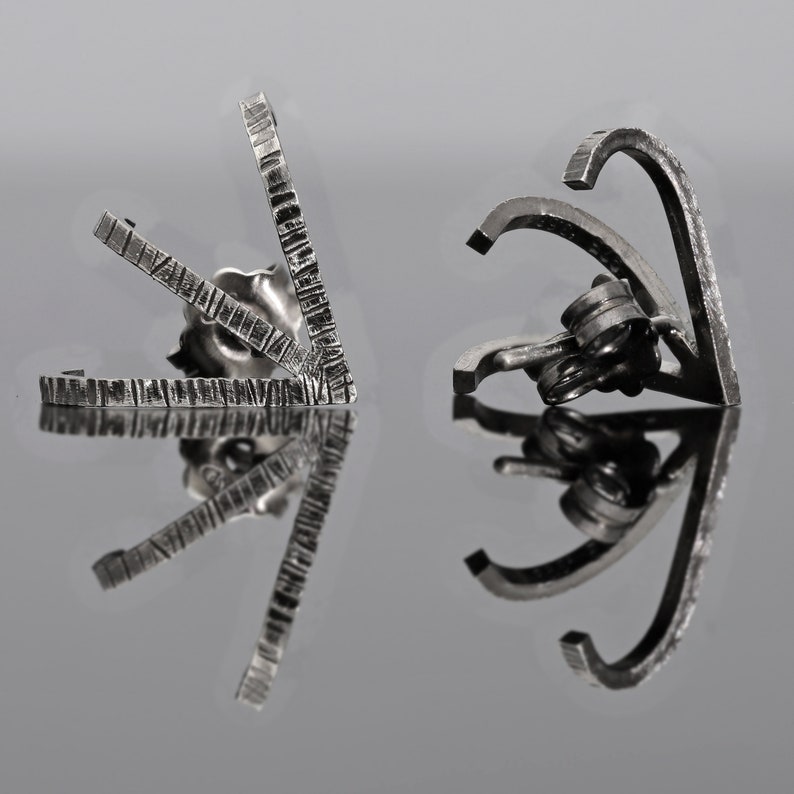May include: A pair of silver earrings with geometric designs. The earrings are made of metal and have a textured finish.