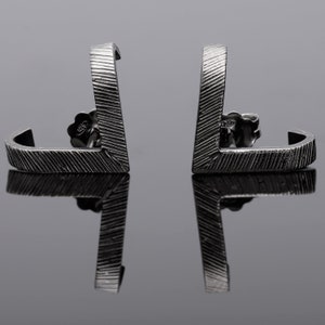 May include: A pair of silver earrings with a geometric design. The earrings are made of a textured metal and have a simple, modern look.