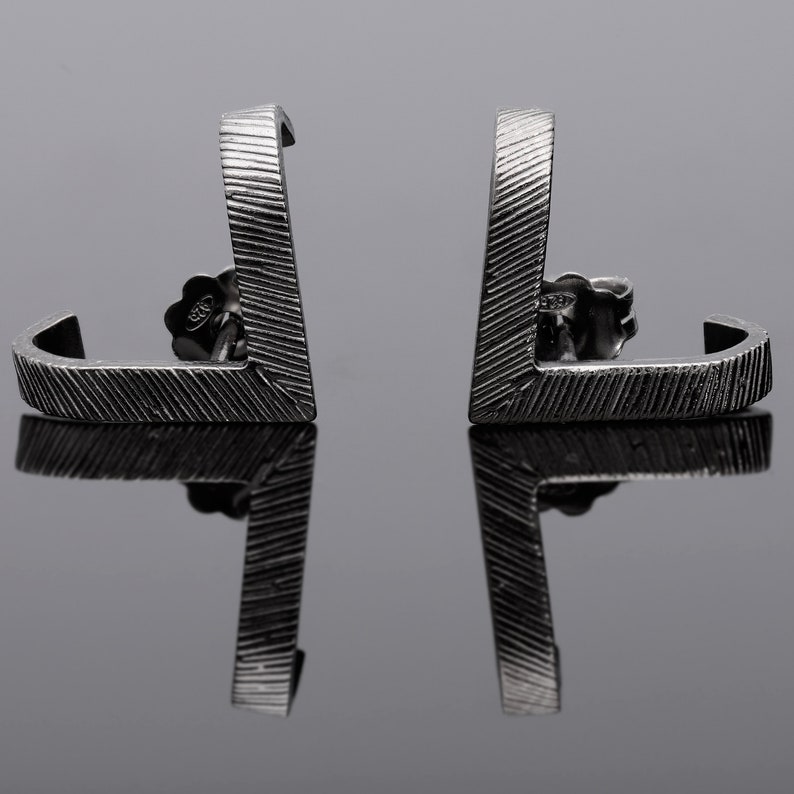May include: A pair of silver earrings with a geometric design. The earrings are made of a textured metal and have a simple, modern look.