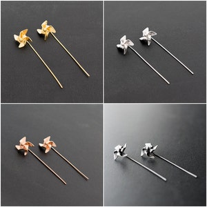 May include: Four pairs of pinwheel-shaped earrings in gold, silver, and rose gold tones. Each earring features a pinwheel design atop a long, slender post. The earrings are displayed against a dark grey background.