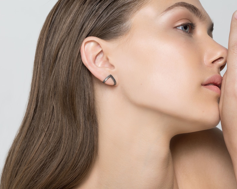 May include: A pair of silver triangle shaped earrings with a black oxidized finish.