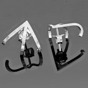May include: A pair of silver earrings with a geometric design. The earrings are made of thin, textured metal and have a simple, modern look.