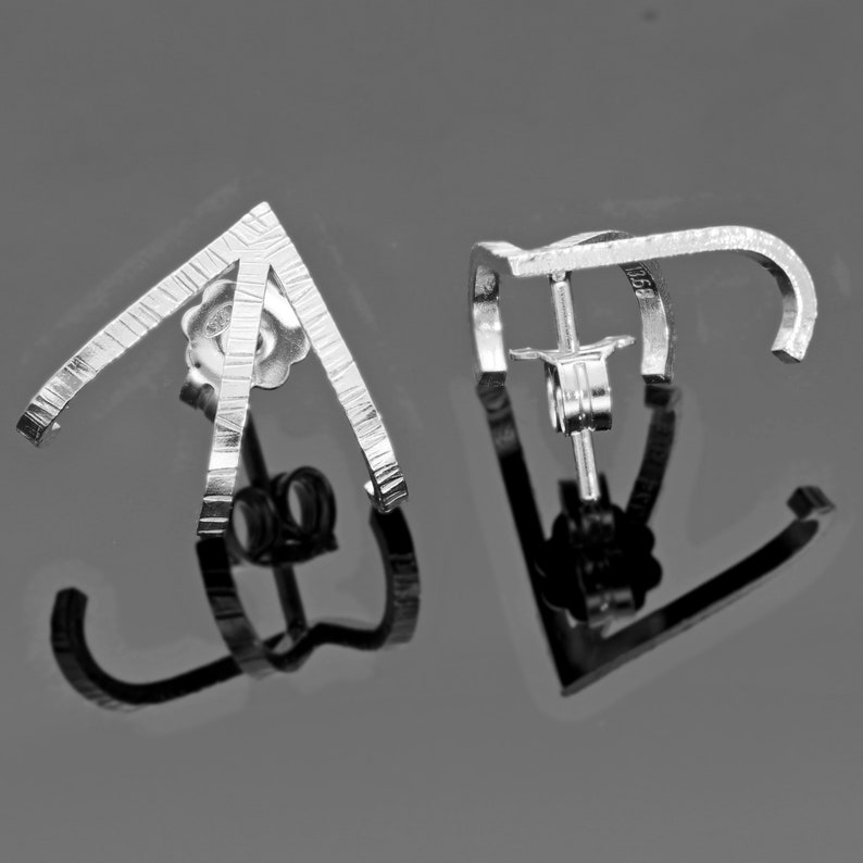 May include: A pair of silver earrings with a geometric design. The earrings are made of thin, textured metal and have a simple, modern look.