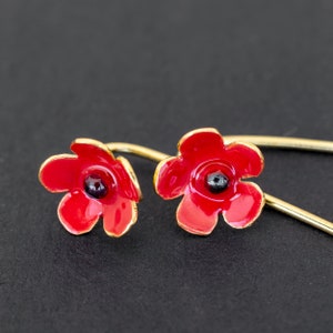 May include: A pair of red poppy flower earrings with gold-toned hooks. The earrings are made of enamel and have a black centre.