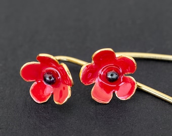 May include: A pair of red poppy flower earrings with gold-toned hooks. The earrings are made of enamel and have a black center.