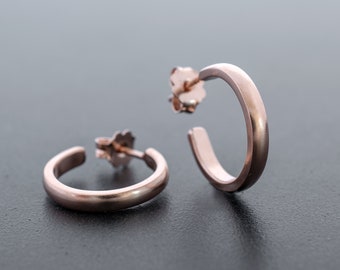 Könnte beinhalten: Ein Paar Ohrringe aus Roségold. Die Ohrringe sind schlicht und elegant, mit einer glatten, polierten Oberfläche.