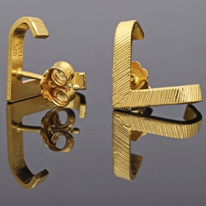 May include: A pair of gold earrings with a geometric design. The earrings are made of 925 silver and are marked with the number 1958.