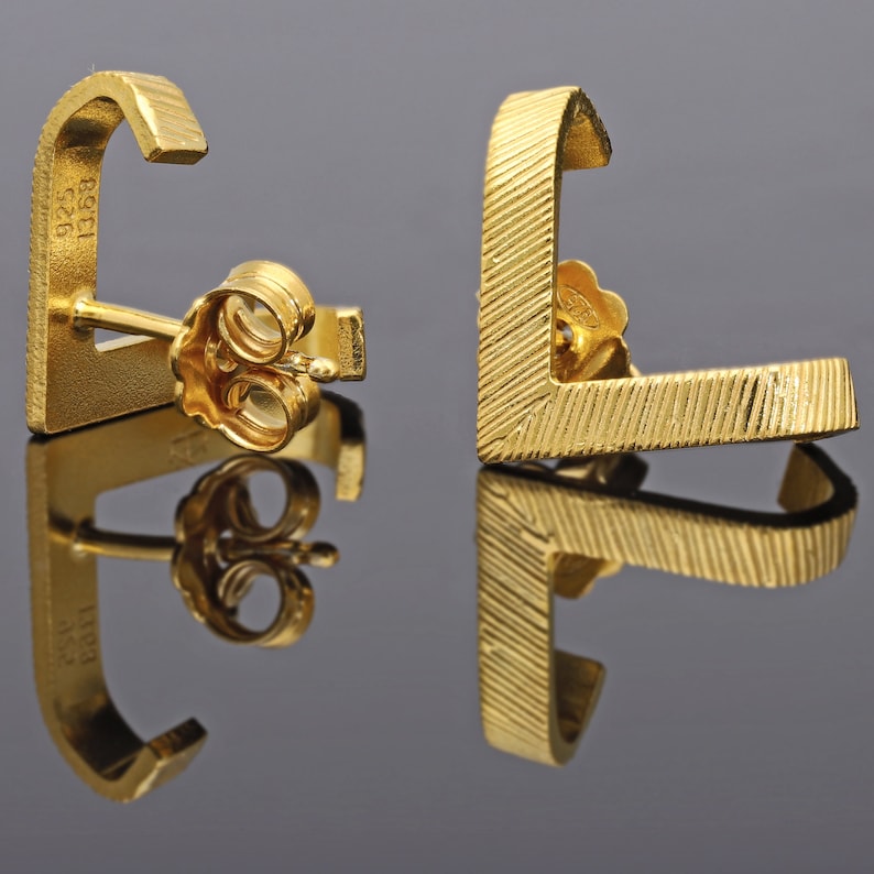 May include: A pair of gold earrings with a geometric design. The earrings are made of 925 silver and are marked with the number 1958.