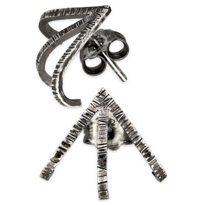 May include: A pair of silver earrings with a geometric design. The earrings are made of two pieces, one a curved shape and the other a triangle shape. Both pieces have a textured surface.