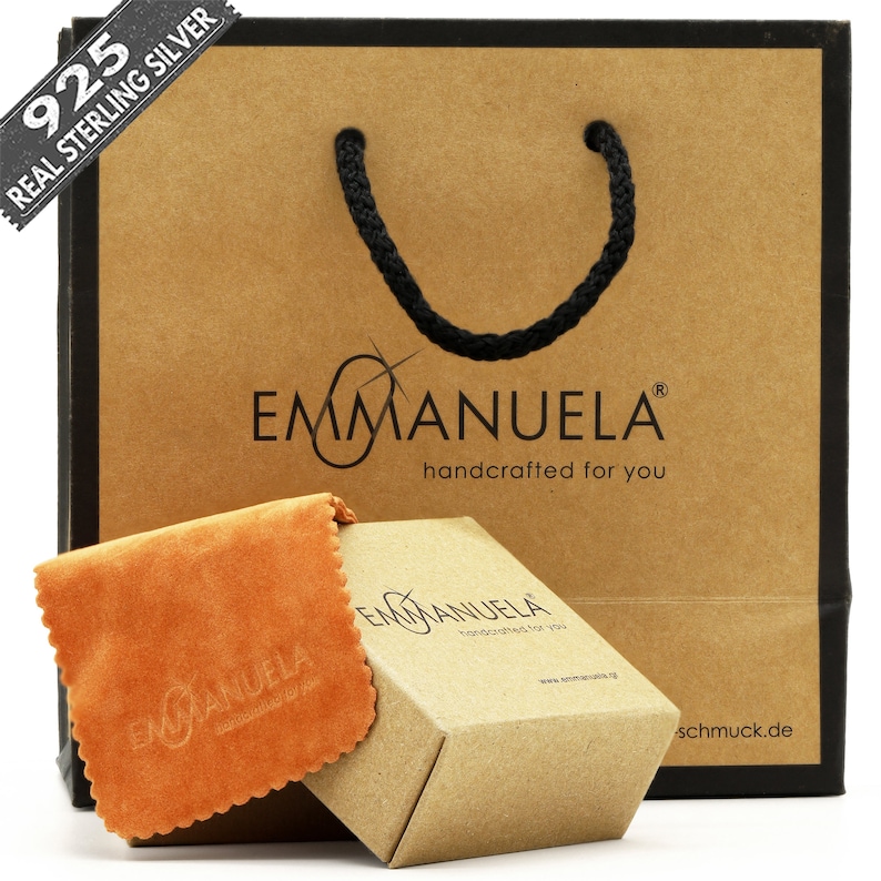 May include: A brown paper gift bag with black handles and the text "925 REAL STERLING SILVER" on the front. The bag is decorated with a brown box and a brown and orange cloth. The box and cloth both have the text "EMMANUELA handcrafted for you" on them.