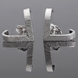 May include: A pair of silver earrings with a geometric design. The earrings are made of a textured metal and have a simple, modern look.