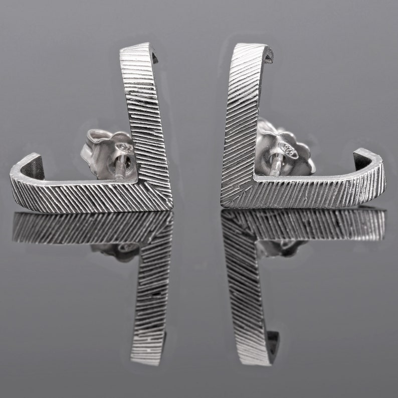 May include: A pair of silver earrings with a geometric design. The earrings are made of a textured metal and have a simple, modern look.