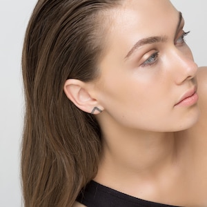 May include: A woman with long brown hair wearing a black top and a small, geometric diamond earring in her left ear.