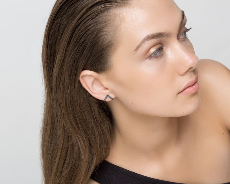 May include: A woman with long brown hair wearing a black top and a small, geometric diamond earring in her left ear.