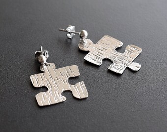 May include: A pair of silver puzzle piece earrings. The earrings are textured and have a brushed finish.