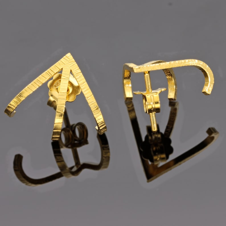 May include: A pair of gold earrings with a geometric design. The earrings are made of textured metal and have a simple, modern style.