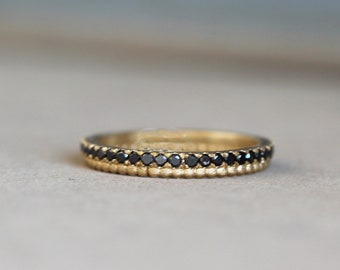May include: A gold band ring with a row of black diamonds around the top edge.