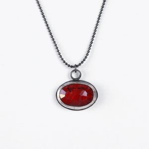 May include: A silver chain necklace with a red gemstone pendant. The pendant is oval shaped and has a silver bezel setting.