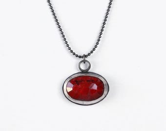 May include: A silver chain necklace with a red gemstone pendant. The pendant is oval shaped and has a silver bezel setting.