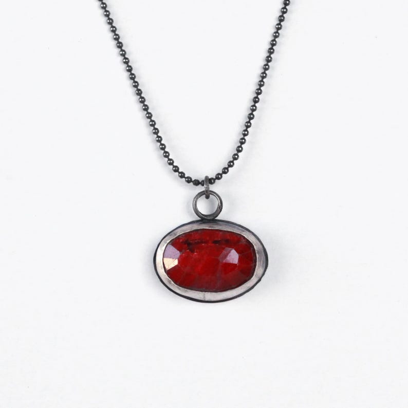 May include: A silver chain necklace with a red gemstone pendant. The pendant is oval shaped and has a silver bezel setting.