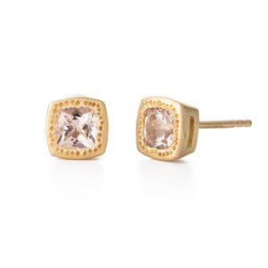 Puede incluir: Un par de pendientes de oro con una piedra preciosa rosa de forma cuadrada engastada en un engaste de oro. Los pendientes tienen un borde de oro texturizado.