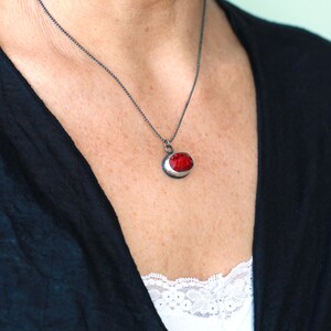 May include: A silver chain necklace with a red and silver pendant. The pendant is oval shaped and has a red stone set in silver.