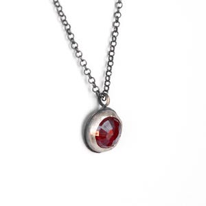 May include: A silver chain necklace with a red gemstone pendant. The pendant is round and has a bezel setting.