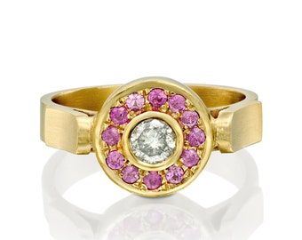 Può includere: Un anello d'oro con una pietra centrale rotonda circondata da un'aureola di zaffiri rosa.