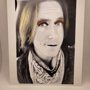 May include: A black and white photograph of a person with long, blonde hair. The person is wearing a bandana with a white and black pattern. The person's eyes are highlighted with colourful makeup.