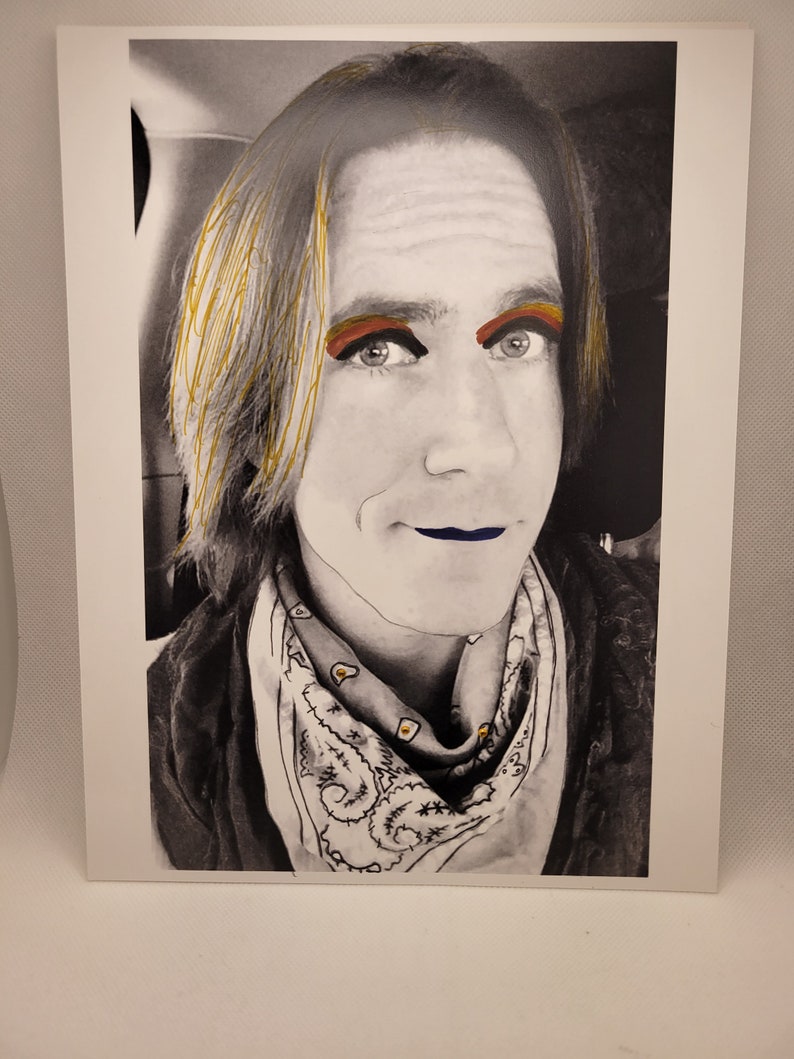 May include: A black and white photograph of a person with long, blonde hair. The person is wearing a bandana with a white and black pattern. The person's eyes are highlighted with colourful makeup.