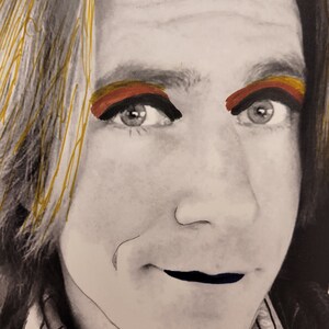 May include: A black and white portrait of a person with gold, red and orange eyeshadow. The person is wearing a black shirt and has a serious expression.