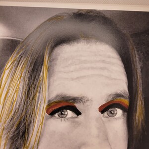 May include: A black and white photograph of a person's face with gold highlights in their hair. The person is wearing red and yellow eyeshadow.