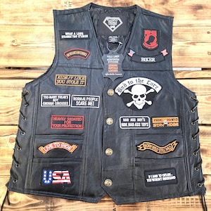 May include: Black leather biker vest with multiple patches. Patches include phrases like "Ride it like you stole it" and "Born Wild Still Wild". The vest has a button-up front and side laces. The vest is made of genuine buffalo leather.