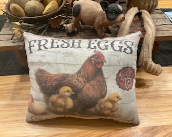 May include: A white pillow with a brown hen and chicks on it. The pillow has the words "Fresh Eggs" printed on it in black letters. There is a red circle with the words "Eggs 25c Doz" printed on it.