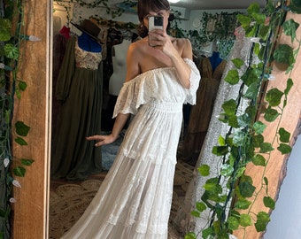 May include: A white off-the-shoulder maxi dress with a tiered skirt and lace detailing. The dress is made of a lightweight fabric and has a relaxed fit.