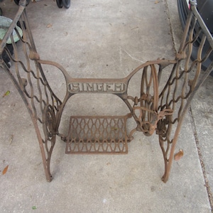 May include: An antique Singer sewing machine base made of cast iron. The base is a dark, rusty brown color with intricate scrollwork and the Singer name prominently displayed. It includes a foot pedal rest.