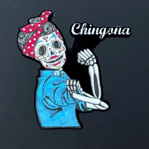 May include: A colorful illustration of a skeleton woman with a red and white polka dot bandana, flexing her bicep. The text "Chingona" is written in black above her.