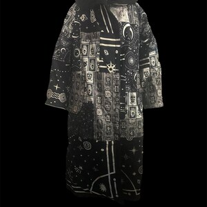 May include: A long, black and white coat with a hood. The coat features a patchwork design with celestial and skull motifs. The hood is trimmed with black faux fur. The coat is floor-length and has long sleeves.