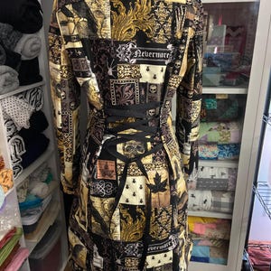 May include: A long-sleeved, patchwork-style coat with a black corset back. The coat features a collage of patterns in black, gold, and cream, including skulls, ornate designs, and the word "Nevermore".