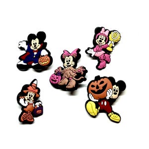 K&ouml;nnte beinhalten: Eine Sammlung von f&uuml;nf Halloween-Schuhanh&auml;ngern mit Mickey- und Minnie-Mouse-Charakteren in verschiedenen Kost&uuml;men. Die Charms zeigen einen Vampir, eine Katze, eine Hexe und Figuren, die K&uuml;rbisse und S&uuml;&szlig;igkeiten halten.