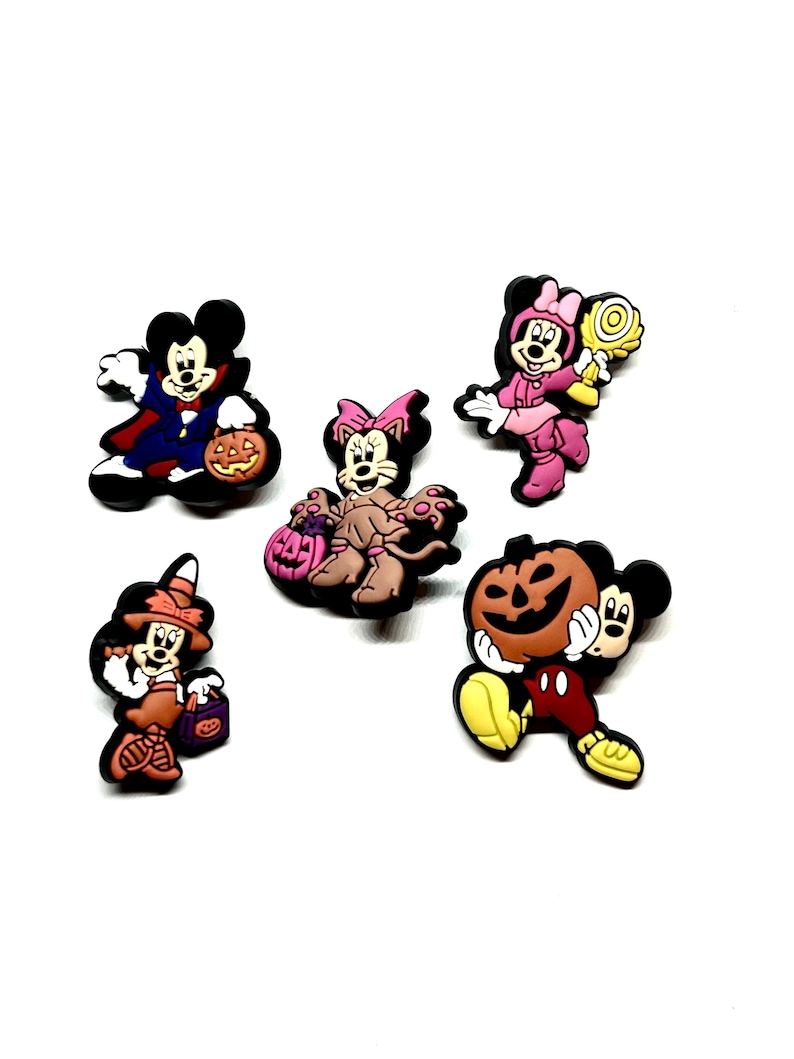 K&ouml;nnte beinhalten: Eine Sammlung von f&uuml;nf Halloween-Schuhanh&auml;ngern mit Mickey- und Minnie-Mouse-Charakteren in verschiedenen Kost&uuml;men. Die Charms zeigen einen Vampir, eine Katze, eine Hexe und Figuren, die K&uuml;rbisse und S&uuml;&szlig;igkeiten halten.