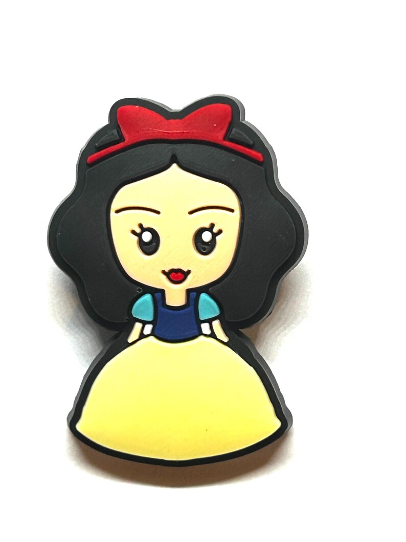 Puede incluir: Una figura de dibujos animados de Blancanieves, con un vestido amarillo, mangas azules y blancas y un lazo rojo. El personaje tiene cabello negro y una expresi&oacute;n sonriente. La imagen es un primer plano sobre un fondo blanco.