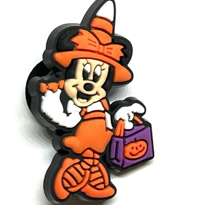 K&ouml;nnte beinhalten: Ein Halloween-Themen-Minnie-Mouse-Charm in Schwarz, Orange, Wei&szlig; und Lila. Minnie ist als Hexe verkleidet, tr&auml;gt einen Hut und h&auml;lt eine S&uuml;&szlig;igkeitent&uuml;te mit einem K&uuml;rbisgesicht. Der Charm hat einen schwarzen Rand.